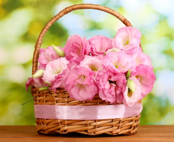 Bouquet of eustoma flowers in basket, on wooden table, on green background — Stock Photo, Image