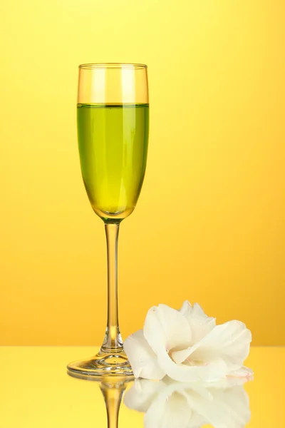 Glass with cocktail and gladiolus bud on yellow background close-up — Stock Photo, Image