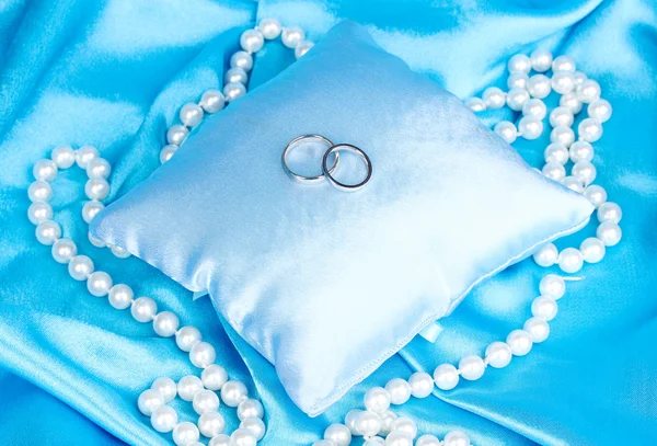 Anillos de boda en almohada de satén sobre fondo de tela azul — Foto de Stock