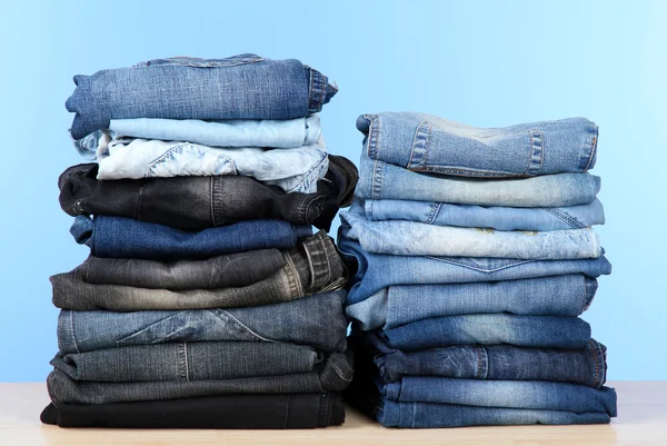 Muitas calças de ganga empilhadas em pilhas no fundo azul — Fotografia de Stock