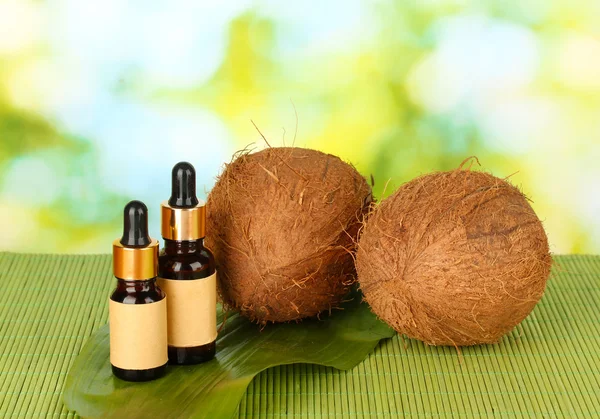 Coconut oil in bottles with coconuts on green background — Stock Photo, Image