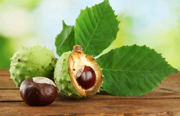 Castanhas com folhas na mesa de madeira em fundo verde — Fotografia de Stock