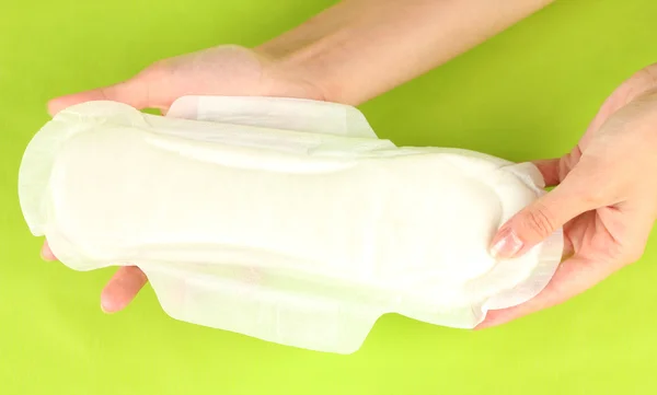 Woman's hands holding a sanitary pad on green background close-up — Stock Photo, Image