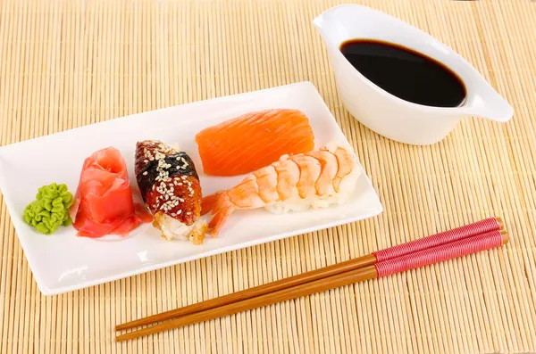Delicious sushi served on plate on bamboo mat — Stock Photo, Image