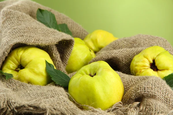 Sweet quinces with leaves, on burlap, on green background — Stock Photo, Image