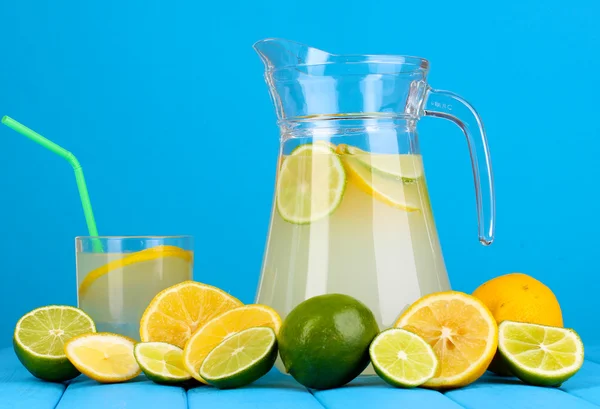 Citrus limonade in werper en glas van citrus rond op houten tafel op blauwe achtergrond — Stockfoto