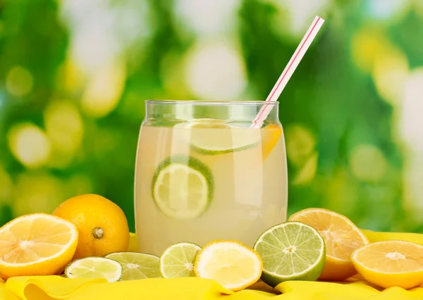 Limonada cítrica en banco de cristal de cítricos alrededor en tela amarilla sobre fondo natural —  Fotos de Stock