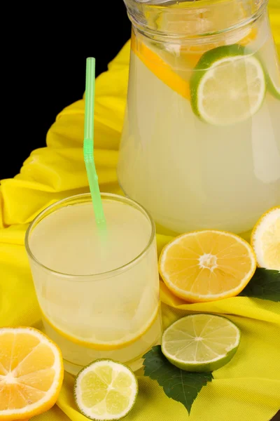 Limonada cítrica en vidrio y jarra de cítricos alrededor en tela amarilla sobre mesa de madera de cerca — Foto de Stock