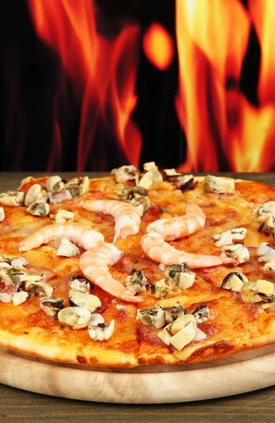 Delicious pizza with seafood on stand on flame background — Stock Photo, Image