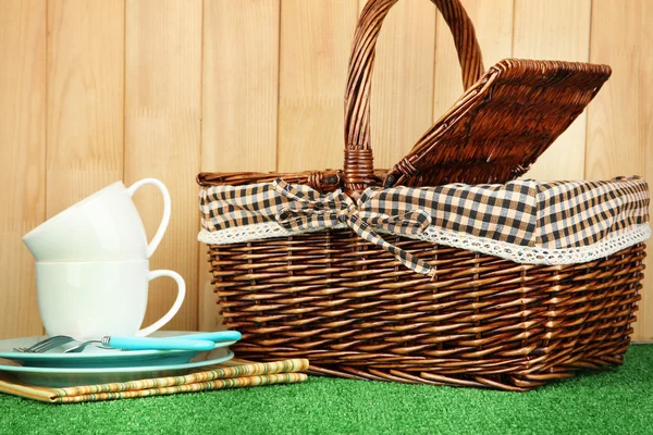 Tazze, piatti e cestino su erba su fondo di legno — Foto Stock