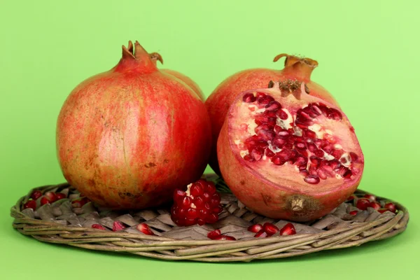 Ripe pomegranates on wicker cradle on green background — Stock Photo, Image