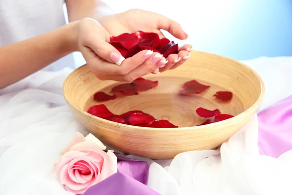 Woman hands with wooden bowl of water with petals, on blue background — Stock Photo, Image