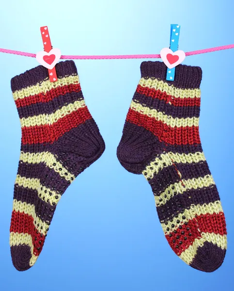 Pair of knit striped socks hanging to dry over blue background — Stock Photo, Image