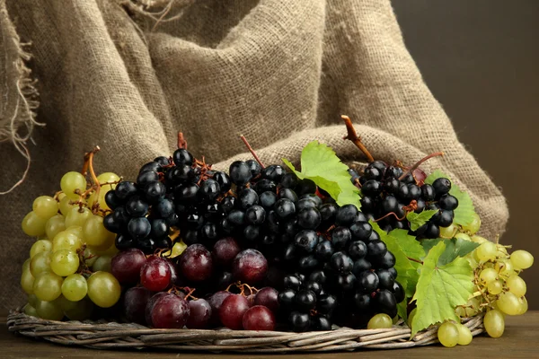 Asortyment dojrzałe słodkie winogrona w koszyku, na brązowym tle — Zdjęcie stockowe