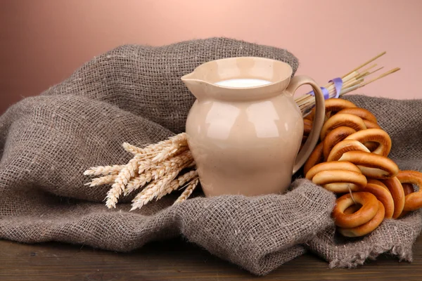 Jar of milk, tasty bagels and spikelets on wooden table, on brown background — Stock Photo, Image