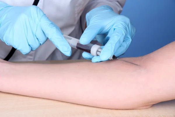 Enfermeira tira sangue das veias em fundo azul — Fotografia de Stock