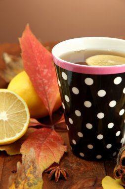 Kahverengi arka planda bir fincan sıcak çay ve sonbahar yaprakları.