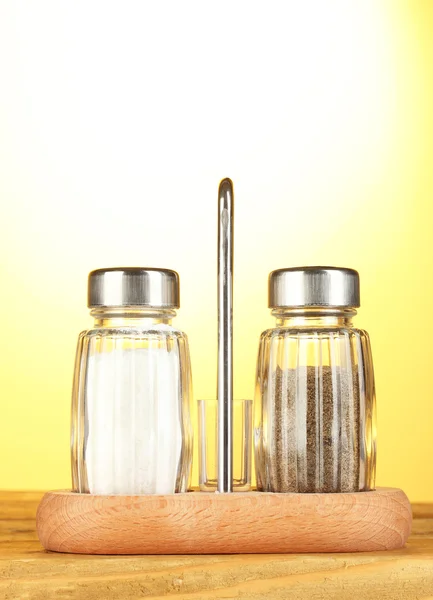 Salt and pepper mills, on wooden table on yellow background — Stock Photo, Image