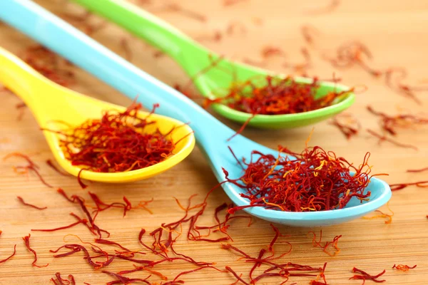 Stigmas of saffron in colorful spoons on wooden background close-up — Stock Photo, Image