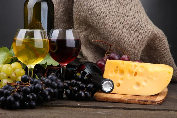 Garrafas e copos de vinho, queijo e uvas sobre fundo cinzento — Fotografia de Stock