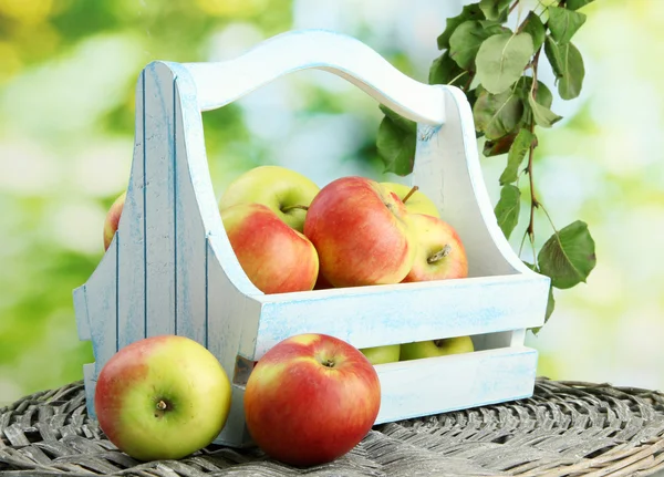 Juicy apples with leaves in wooden basket, on green background — Stock Photo, Image