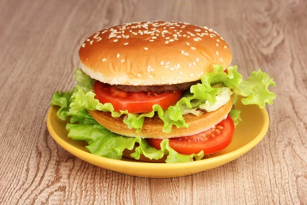 Big and tasty hamburger on plate on wooden table — Stock Photo, Image