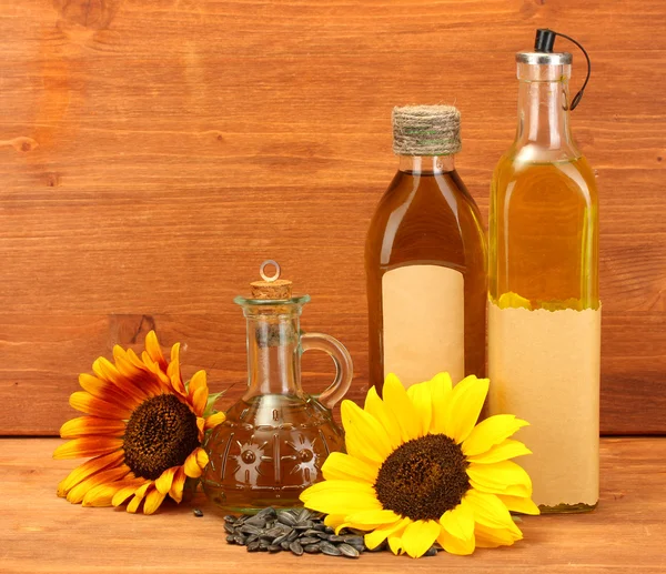 Olie in flessen, zonnebloemen en zaden, op houten achtergrond — Stockfoto