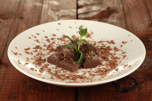 Stukken van chocolade en munt op de plaat op houten achtergrond close-up — Stockfoto