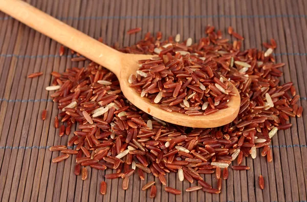 Red rice in wooden spoon on bamboo mat — Stock Photo, Image