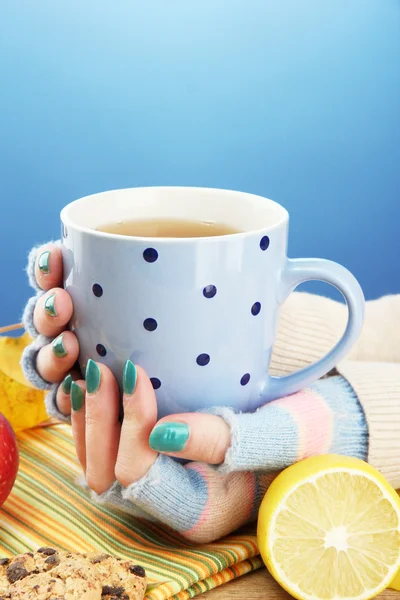 Hands holding cup of hot drink and autumn leaves, on blue background — Stock Photo, Image