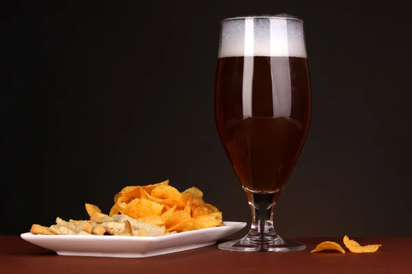 Стакан пива с крекерами и чипсами на коричневом фоне — стоковое фото