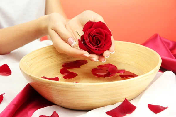 Woman hands with wooden bowl of water with petals, on red background Royalty Free Stock Images