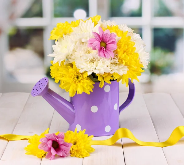 Purple watering can of peas with flowers on white wooden table on window background — Stock Photo, Image