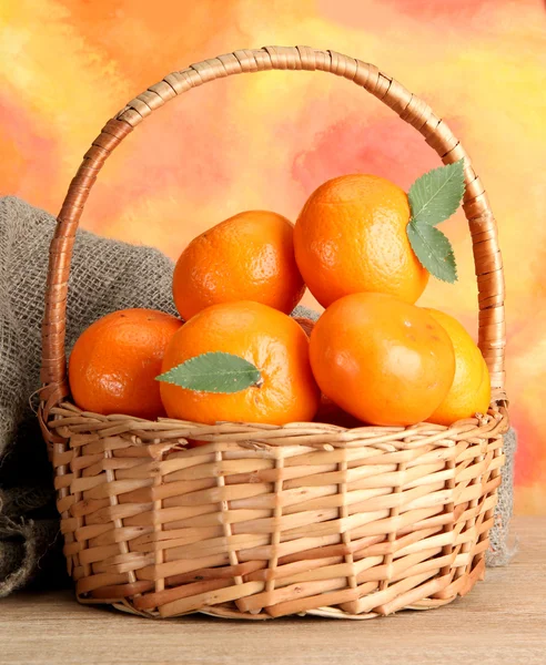 Tangerines with leaves in a beautiful basket, on wooden table on orange background — Stock Photo, Image