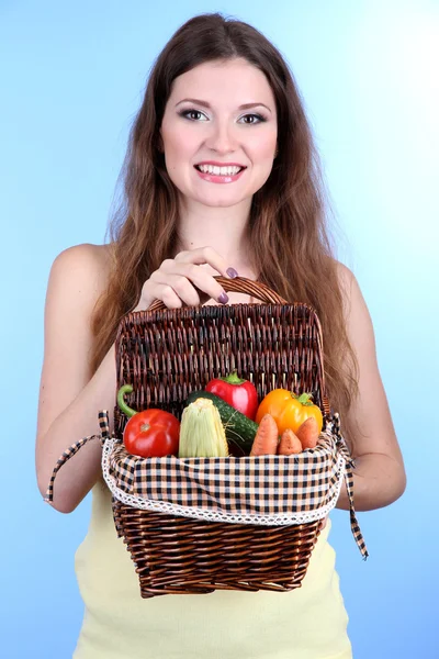 Mooie vrouw met groenten in rieten mand op blauwe achtergrond — Stockfoto