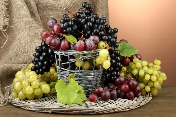 Assortment of ripe sweet grapes in basket, on brown background — Stock Photo, Image