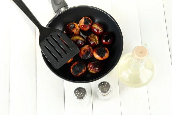 Roasted chestnuts in the pan and decanter with oil, salt and pepper on white wooden background — Stock Photo, Image