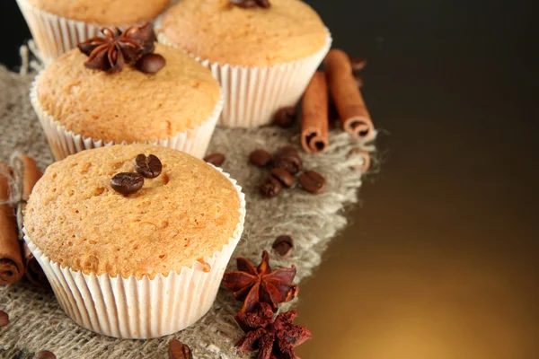 Tasty muffin cakes on burlap, spices and coffee seeds, on brown background — Zdjęcie stockowe