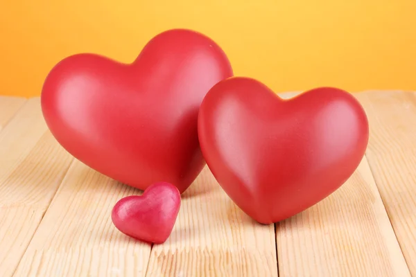 Corazones rojos decorativos sobre mesa de madera sobre fondo naranja — Foto de Stock