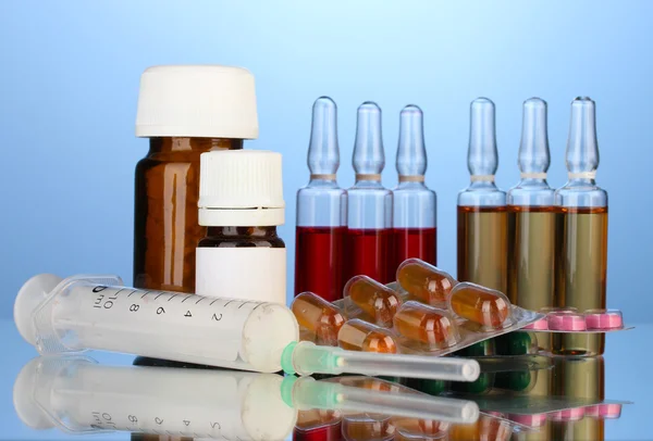 Медицинские ампулы, бутылки, таблетки и шприцы на синем фоне — стоковое фото