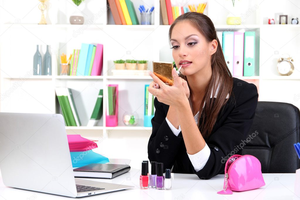 young business woman looking in the mirror and using lipstick at her worlplace