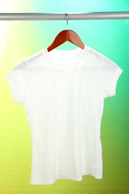 Askı üzerinde yeşil bir arka plan üzerinde beyaz t-shirt