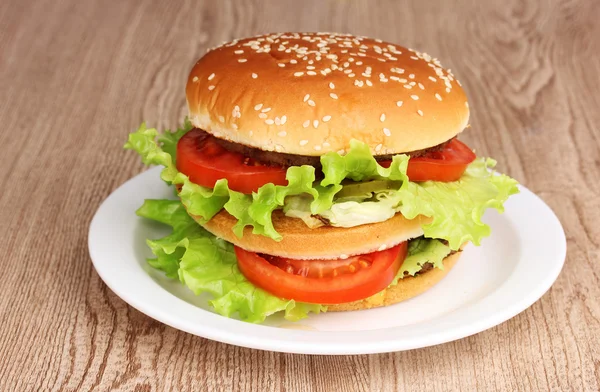 Grand et savoureux hamburger sur assiette sur table en bois — Photo