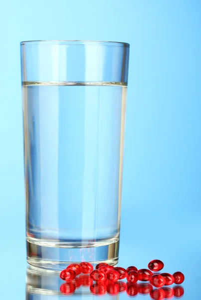 A glass of water and pills on blue background close-up — Stock Photo, Image