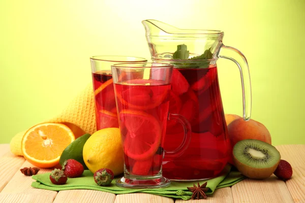 Sangria im Glas und Glas mit Früchten, auf Holztisch, auf grünem Hintergrund — Stockfoto