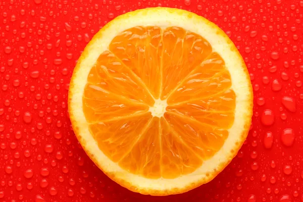 Slice of orange with drop on red background — Stock Photo, Image