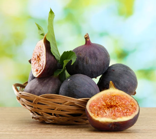 Ripe sweet figs with leaves in basket, on wooden table, on green background — Stock Photo, Image