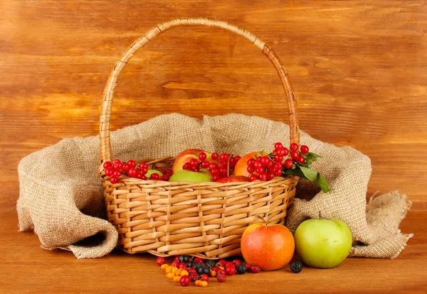 crop of berries and fruits in a basket on wooden background close-up