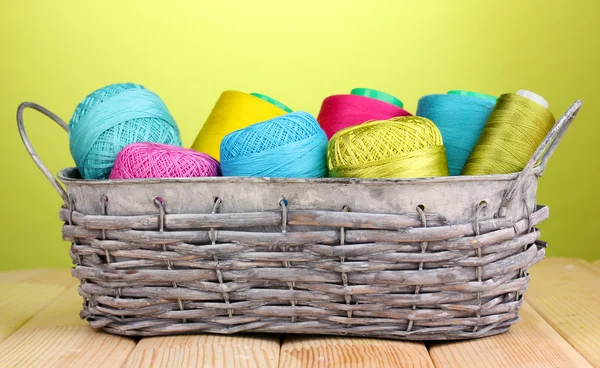 Bright threads in basket on wooden table on green background — Stock Photo, Image