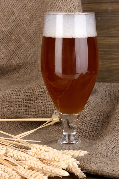 Vaso de cerveza sobre mesa de madera sobre fondo de saco —  Fotos de Stock